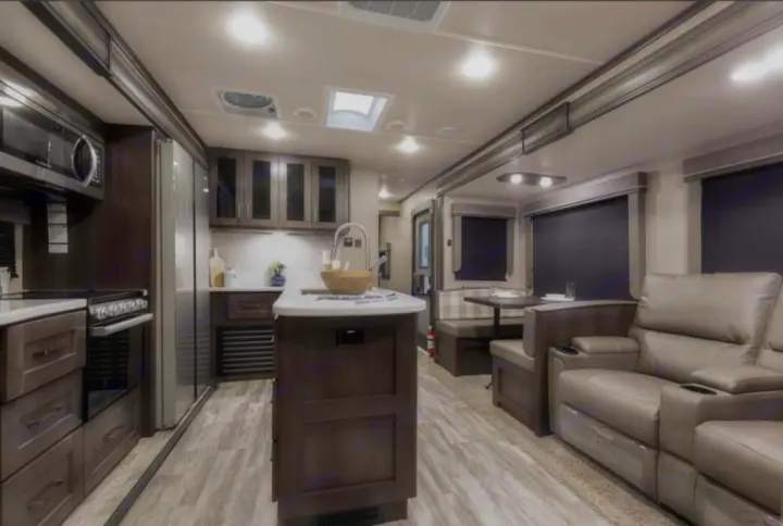 Explore this modern RV rental interior featuring a full kitchen island, dining booth, and reclining living room sofas.. Grand Design Reflection 2022