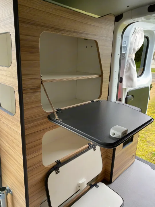 RV rental camper van interior: sleek wooden storage, open shelves, and a flip-down table with light/USB module.. Renault TRAFIC 2023