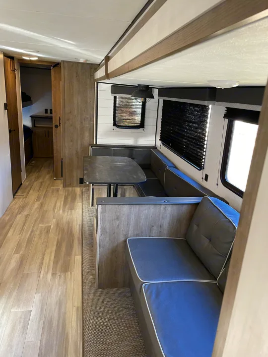 Modern rv rental interior with a spacious dinette, sleek wood-look flooring, and bright windows. Ready for travel adventures!. Heartland RVs Pioneer 2021