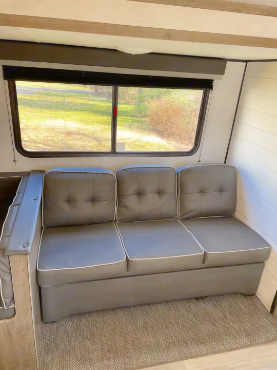 Cozy RV rental interior: A comfortable gray couch by a window overlooking greenery. Ideal for your next RV adventure.. Heartland RVs Pioneer 2021