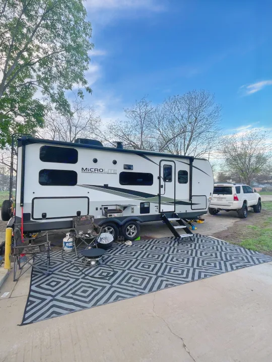 A well-appointed RV rental setup: Micro Lite travel trailer with outdoor rug, grill, and camping chairs ready for adventure.. Flagstaff Microlite 2023
