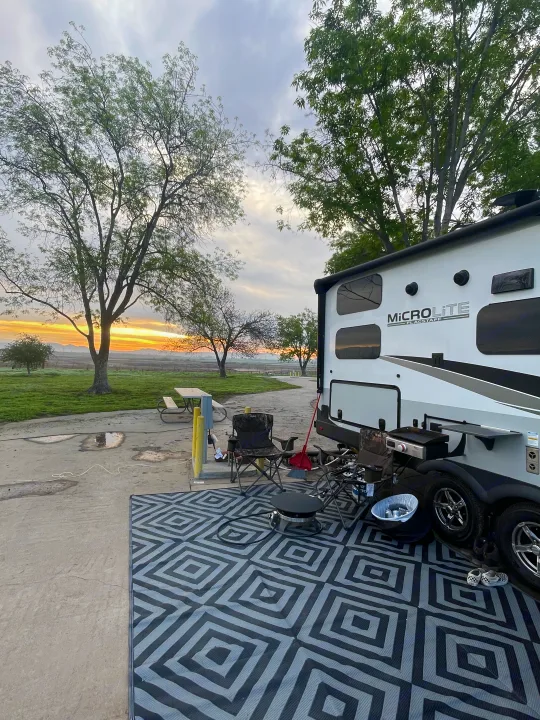 RV rental at campsite: Micro Lite trailer with outdoor setup (mat, grill, chairs) against a vibrant sunset.. Flagstaff Microlite 2023
