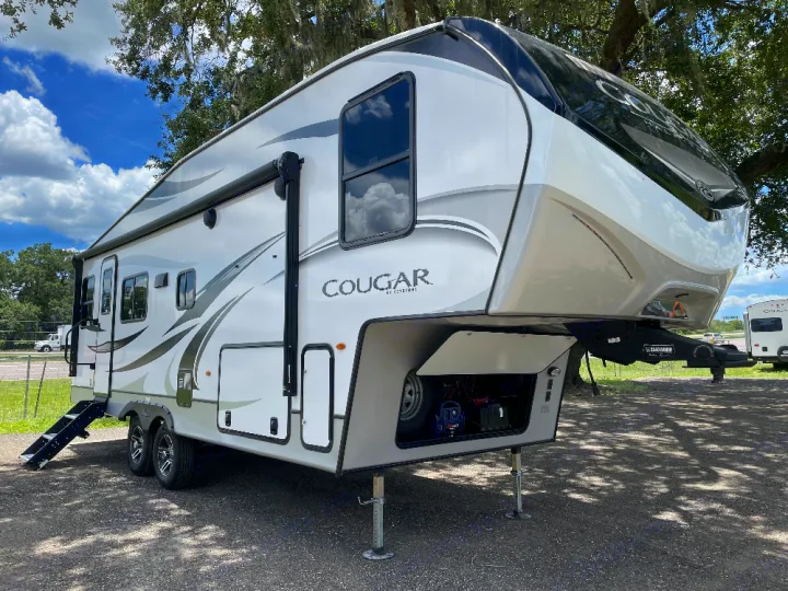 Spacious white and gray fifth-wheel RV, ideal for an RV rental. Parked outdoors with a front storage compartment open.. Keystone Cougar 2022