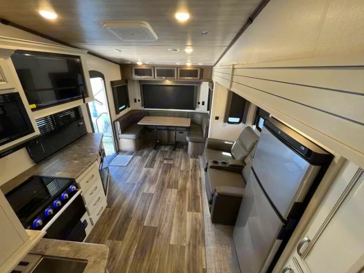 Bright rv rental interior featuring a kitchen with stove, microwave, dinette, and recliners, all with wood-look flooring.. Keystone Cougar 2022