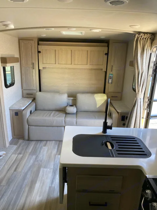 Bright RV rental interior showing a light wood-look kitchen/dinette area, grey cushions, and a sliding door.. Flagstaff Microlite 2023