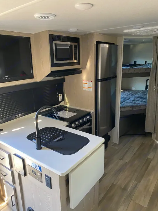 Modern rv rental interior: compact kitchen with stainless steel appliances (fridge, microwave, stove, sink) and cozy sleeping area.. Flagstaff Microlite 2023