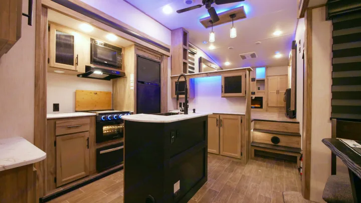 Modern RV rental interior with blue accent lighting, showcasing a full kitchen (stove, microwave, fridge) & living area.. Forest River Cherokee Arctic Wolf 2022
