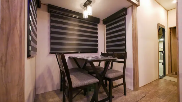 RV rental interior: cozy dining area with table, four dark chairs, and stylish striped blinds. Light fixture above.. Forest River Cherokee Arctic Wolf 2022