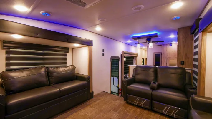 Spacious RV rental living area featuring dark leather recliners & sofa, blue accent lighting, and wood-look floors.. Forest River Cherokee Arctic Wolf 2022