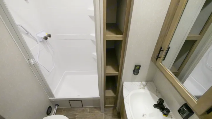 Compact RV rental bathroom with white shower, sink vanity, mirrored cabinet, and open shelving for efficient use of space.. Forest River Cherokee Arctic Wolf 2022
