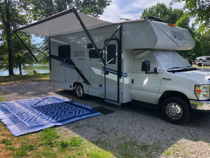 RV rental with extended awning and outdoor mat, parked at a scenic lakeside campsite.. Forest River Coachmen Cross Trail XL 2022