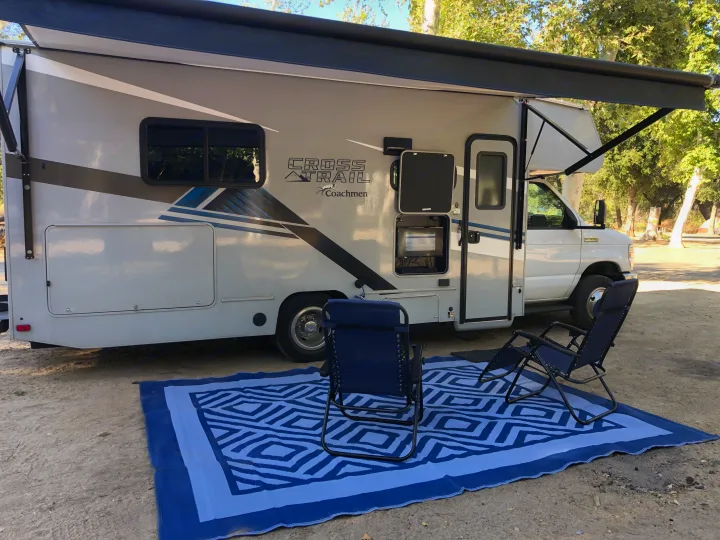 Enjoy your RV rental adventure! A Coachmen Cross Trail RV with extended awning, outdoor mat, and chairs at a sunny campground.. Forest River Coachmen Cross Trail XL 2022