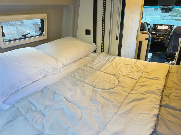 An RV rental's cozy interior featuring a bed, window, and view into the driver's cab.. Winnebago Revel 2020