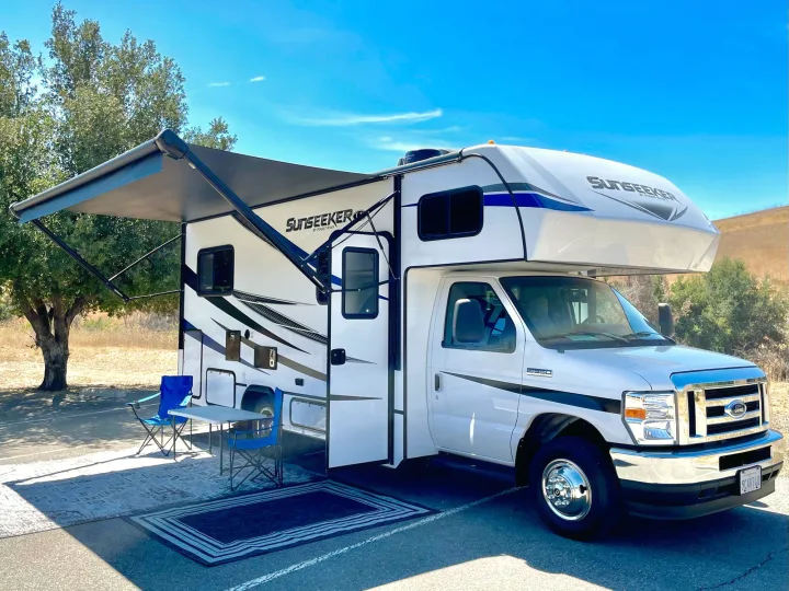 Spacious RV rental set up with an extended awning, chairs, and table at a sunny outdoor campsite.. Forest River Sunseeker 2022