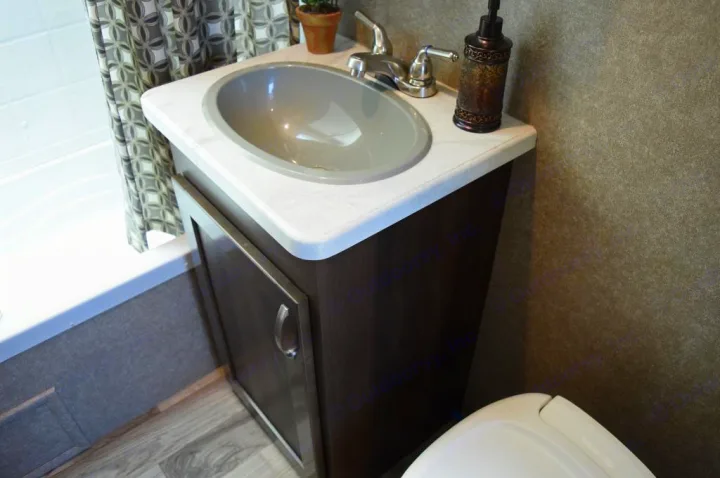 RV rental bathroom: A dark wood vanity with a gray oval sink, chrome faucet, and soap dispenser. Toilet and shower curtain visible.. Jayco Octane 2018