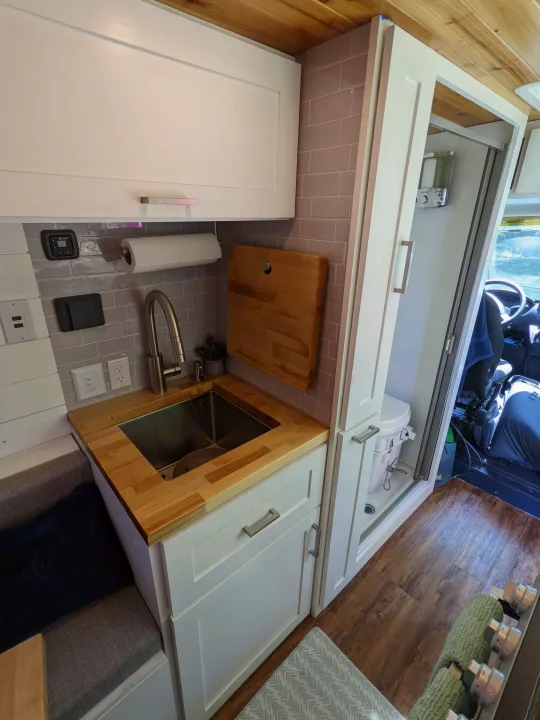 RV rental interior: modern kitchen with sink, tiled backsplash, and a hidden shower/toilet, plus a cozy seating area.. RAM Promaster 2019