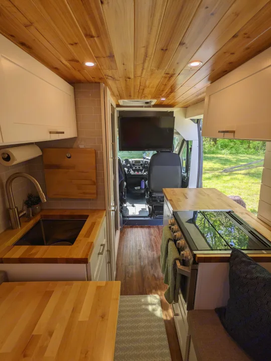 Step inside this cozy RV rental with natural wood ceilings & countertops. A full kitchen, living space, and front cabin area are visible.. RAM Promaster 2019