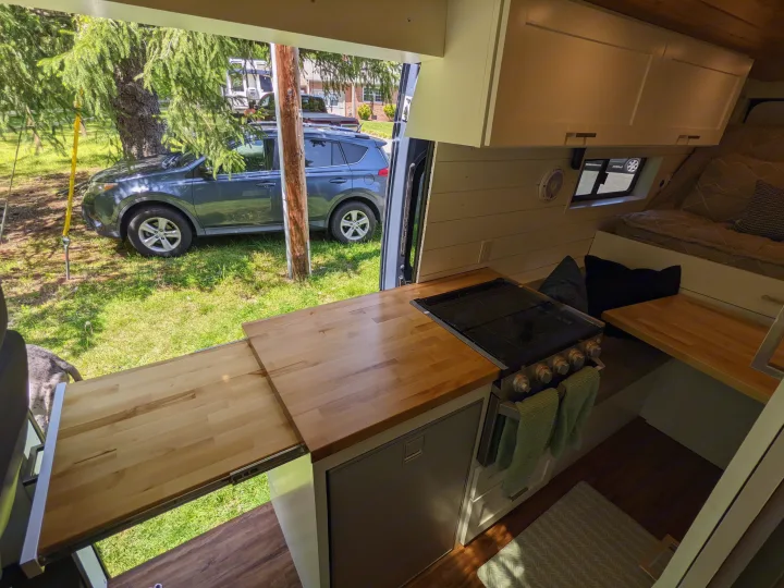 RV rental view from inside: stylish campervan interior with kitchen, bed, and custom extendable counter, overlooking a yard.. RAM Promaster 2019