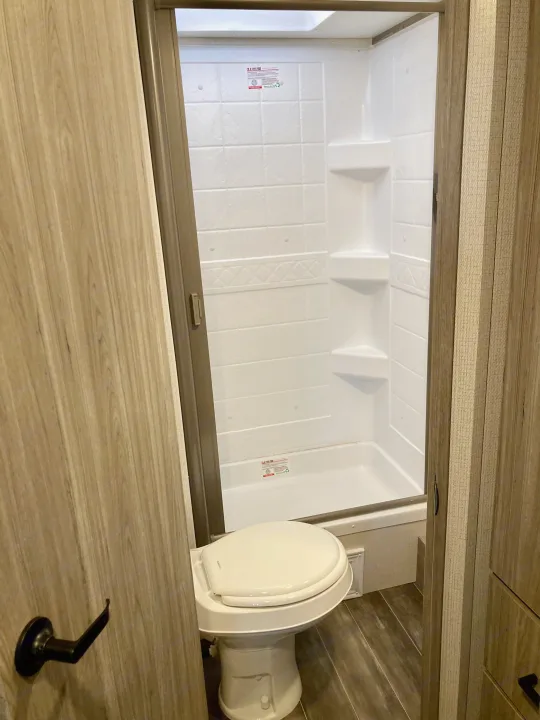 An RV rental's compact bathroom, showing a white toilet, enclosed shower stall with skylight, and wood paneling.. Keystone RV Passport SL 2022