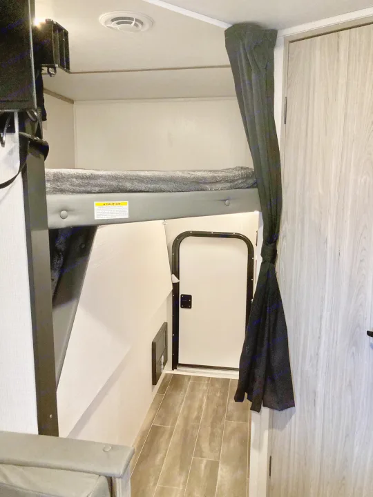 RV interior features a cozy bunk bed above a small access door. Ideal for rv rental adventures.. Keystone RV Passport SL 2022