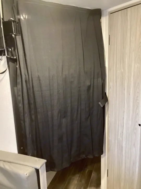 Inside an RV rental: a dark room-dividing curtain beside a light wood door, and seating, offering privacy in the space.. Keystone RV Passport SL 2022