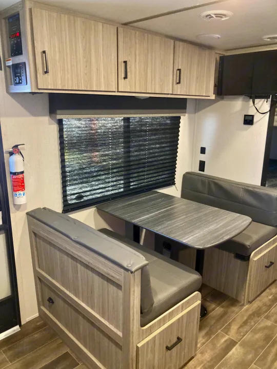 RV rental interior: A well-appointed dinette with table and benches, overhead cabinets, system controls, and a mounted TV.. Keystone RV Passport SL 2022