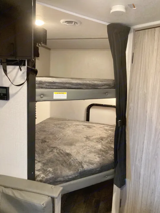 Interior of an RV rental showing two bunk beds with grey mattresses, a mounted TV, and ceiling safety devices.. Keystone RV Passport SL 2022