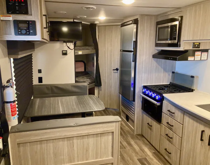 RV rental interior features a full kitchen (stove, microwave, fridge), dinette, bunk beds, and wood finishes.. Keystone RV Passport SL 2022