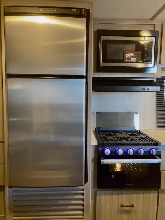 RV rental kitchen: stainless steel fridge, microwave, and gas stove with cool blue illuminated knobs, a complete cooking setup.. Keystone RV Passport SL 2022