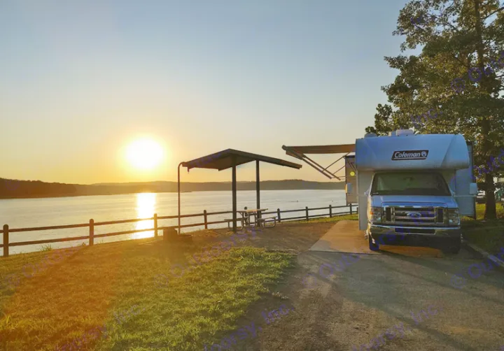 An RV rental overlooks a beautiful lake sunset at a serene campsite with a picnic area.. Thor Coleman 2021