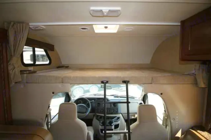 Interior of an RV rental, showcasing the cab-over bunk bed, driver's area, and ladder. Perfect for camper trips.. Thor Coleman 2021