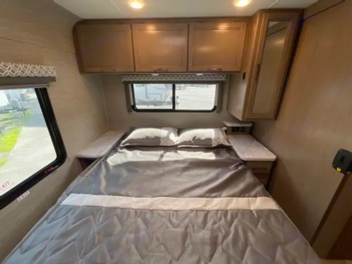 RV rental bedroom: Comfortable bed, overhead storage, side tables, and a mirrored cabinet near windows.. Thor Coleman 2021