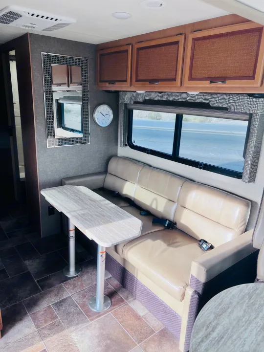 RV rental interior: cozy dining area with couch, table, overhead cabinets, window view, and tiled floor.. Thor Vegas 2017
