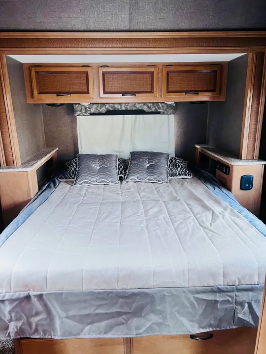 Cozy RV rental bedroom: queen bed with grey pillows, wood cabinets, and integrated nightstands with outlets.. Thor Vegas 2017