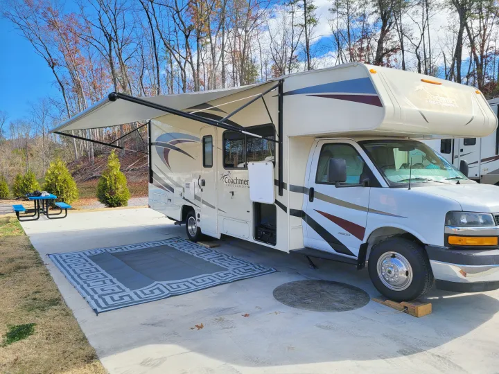 A white Coachmen Freelander RV rental at a sunny campsite with awning, outdoor mat, and picnic table.. Coachman Freelander 2019