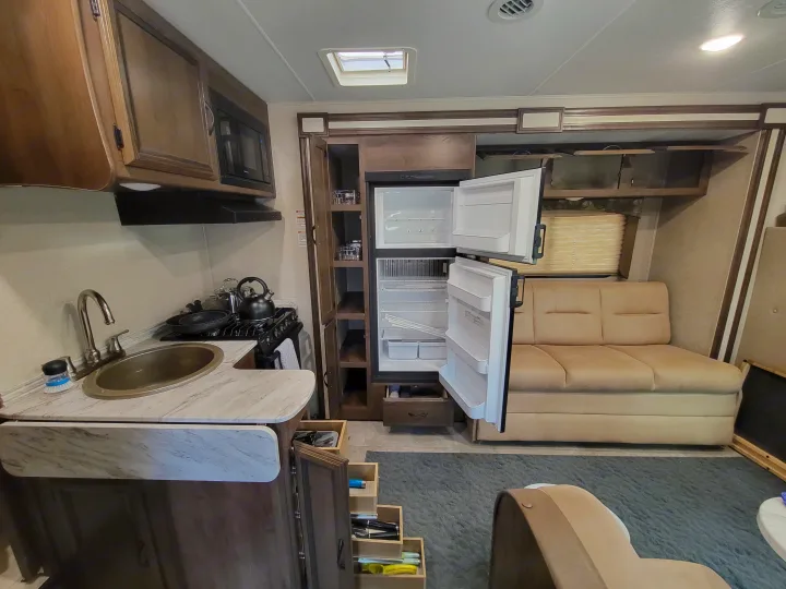 This RV rental features a compact kitchen with a stove, sink, and fridge, plus a cozy living area with a sofa.. Coachman Freelander 2019