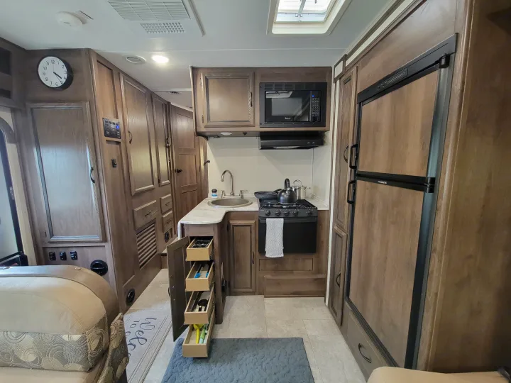 RV rental's warm wood interior: a full kitchen with microwave, stove, sink, and fridge, plus a sofa.. Coachman Freelander 2019