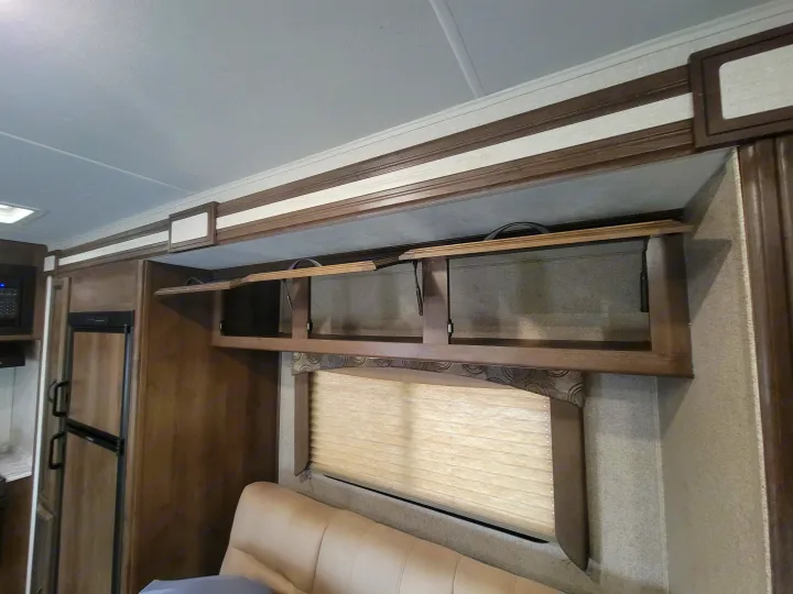 Experience an RV rental: Compact living space featuring open overhead cabinets, a window with blinds, and kitchen appliances.. Coachman Freelander 2019