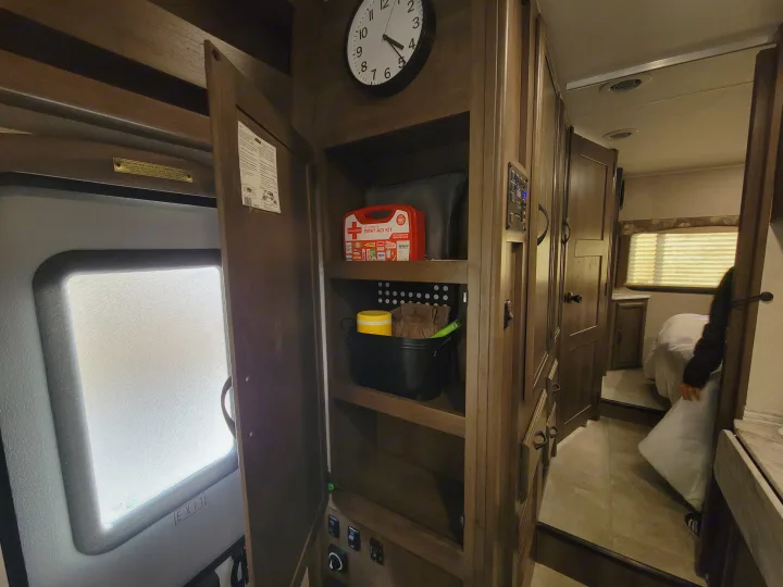 Cozy RV rental interior with an open cabinet displaying a first aid kit, system controls, and a compact bedroom.. Coachman Freelander 2019