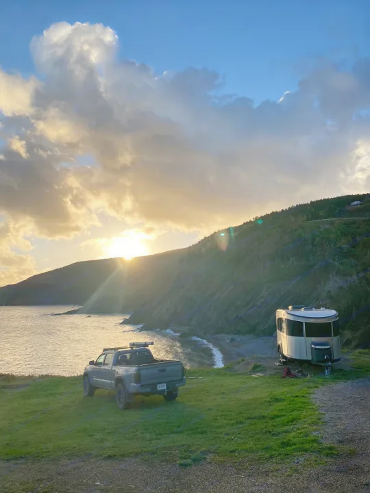 Beautiful sunset RV rental camping overlooking a scenic rocky coast. Truck and trailer parked by the ocean.. Airstream Basecamp 2022