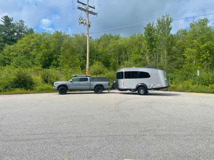 A grey truck tows a modern silver travel trailer. Consider this sleek RV rental for your next outdoor adventure.. Airstream Basecamp 2022