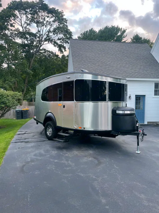 An Airstream travel trailer, a compact RV rental option, is parked on a home's driveway.. Airstream Basecamp 2022