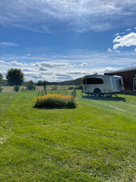 Relaxing RV rental getaway: A travel trailer parked in a lush green field with yellow flowers and mountains.. Airstream Basecamp 2022