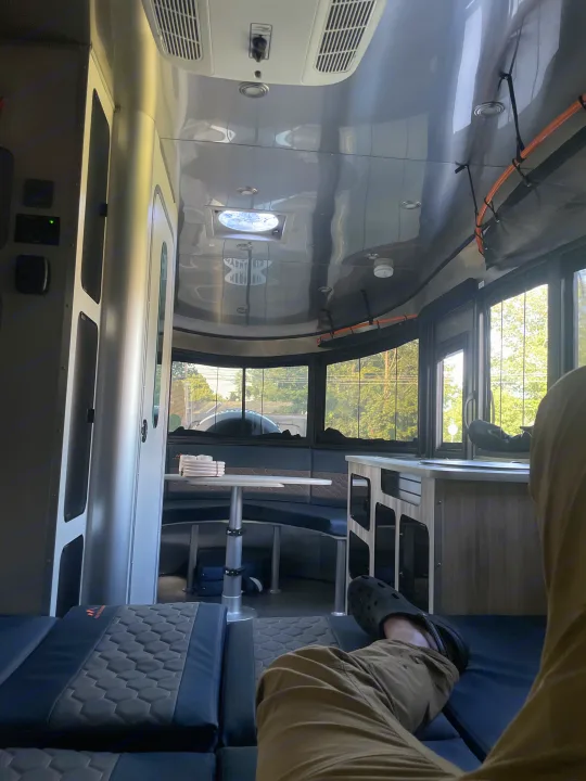 Relaxing in a comfortable RV rental interior. Features modern design, a dining area, and large windows showing nature.. Airstream Basecamp 2022