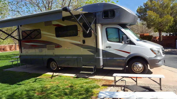Spacious Class C rv rental with an extended awning at a sunny campsite, offering comfortable outdoor living.. Winnebago View 2017