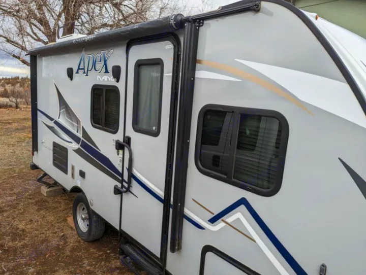 Light gray Apex Nano travel trailer RV rental, with awning extended. Perfect for outdoor adventures, parked in a natural setting.. Coachmen Apex Nano 2019