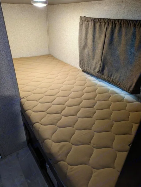 RV rental interior: A compact sleeping area featuring a single bunk bed with a quilted mattress, light walls, and window privacy curtain.. Coachmen Apex Nano 2019
