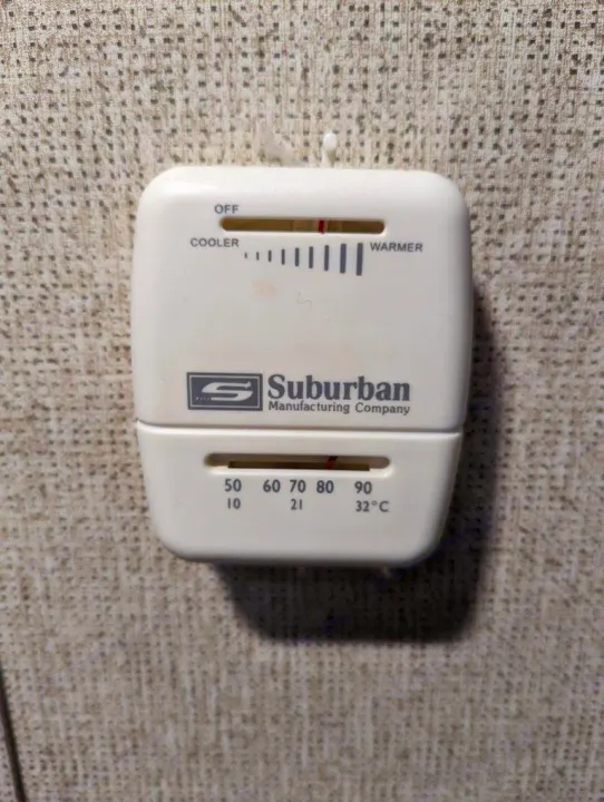 RV rental thermostat (Suburban) on a wall, showing manual slider for cooler/warmer settings and Fahrenheit/Celsius scales.. Coachmen Apex Nano 2019