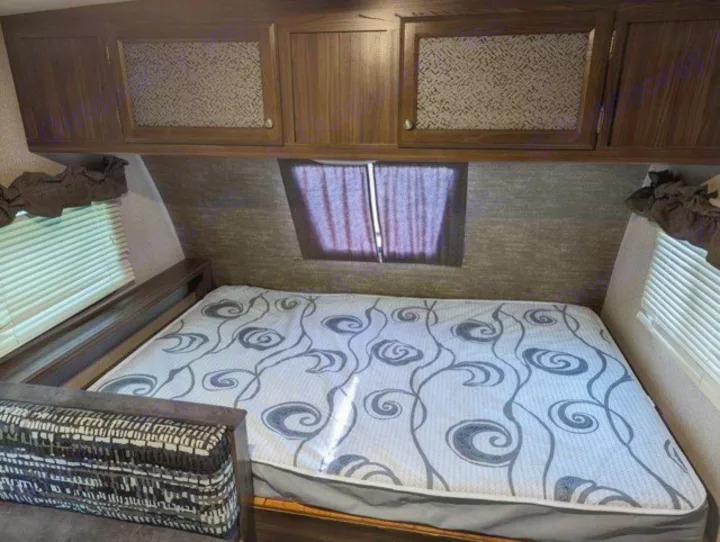 This RV rental interior features a cozy bedroom with a patterned mattress, overhead cabinets, and side windows.. Coachmen Apex Nano 2019