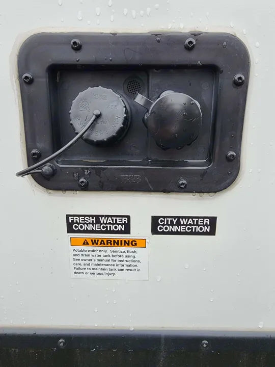 RV exterior panel showing fresh and city water inlets with a warning label for proper tank use, critical for rv rental.. Keystone RV Passport Grand Touring 2018